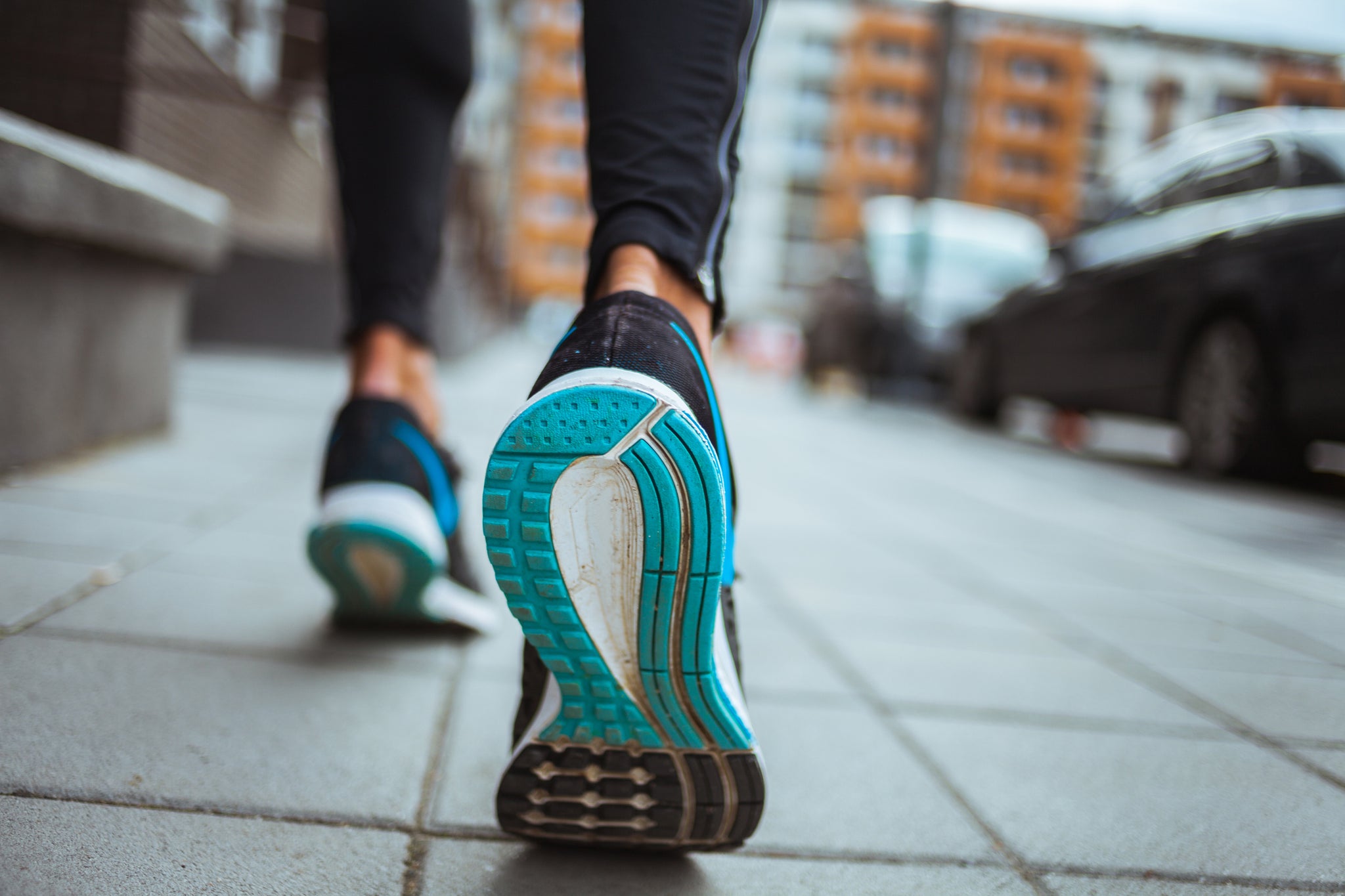 Photo of woman walking down a city street with focus on soles of running sneakers